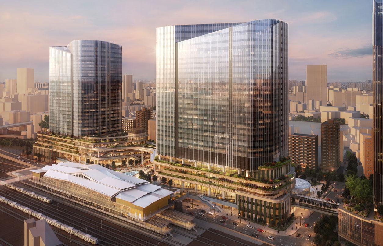 Aerial view of the conceptual rendering of Global Gateway Shinagawa, featuring two modern glass skyscrapers with tiered green rooftops, integrated greenery, and a transportation hub with train tracks in the foreground. The cityscape extends to the horizon, with mountains visible in the background.