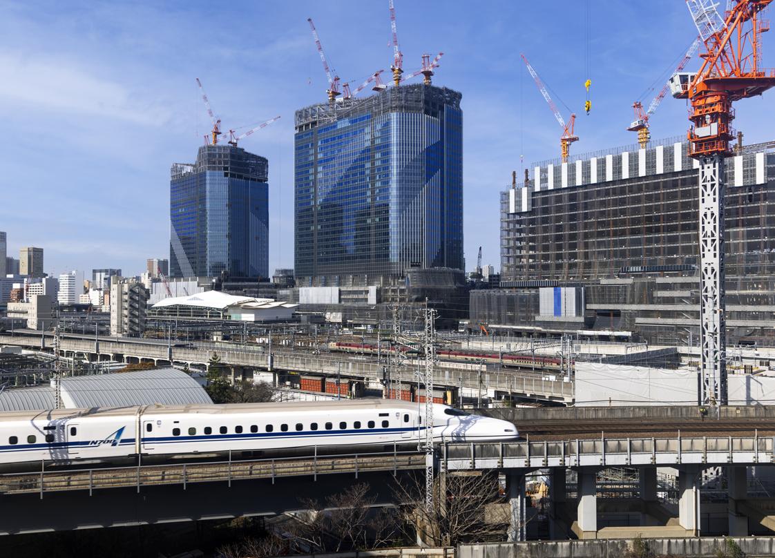 Takanawa Gateway City construction site with multiple skyscrapers, cranes, and a high-speed train on elevated tracks in the foreground