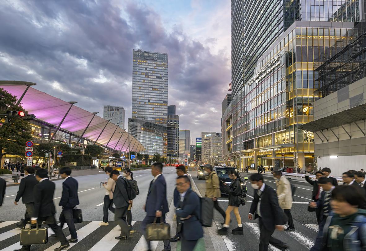 People crossing a street near Tokyo Midtown Yaesu during dusk, with illuminated buildings and a vibrant cityscape in the background.