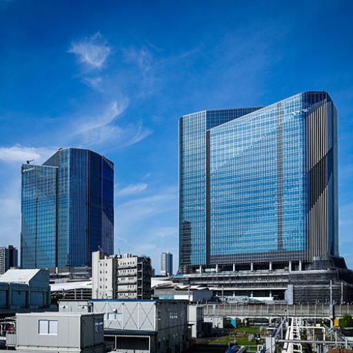 Takanawa Gateway City under construction, featuring tiered, green-roofed buildings with integrated greenery and wide pedestrian stairs, populated with people enjoying the space.